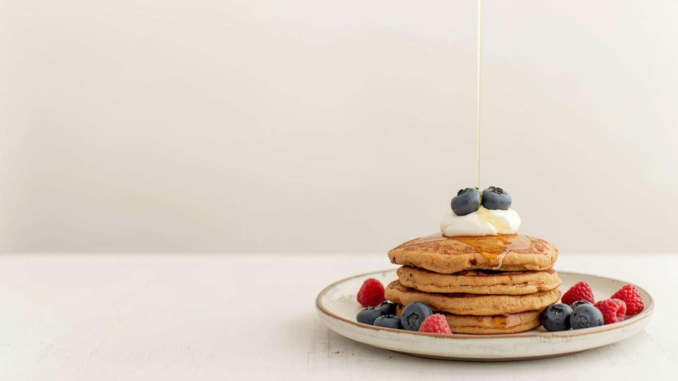 Stack of pancakes with berries and syrup on a plate against a plain background